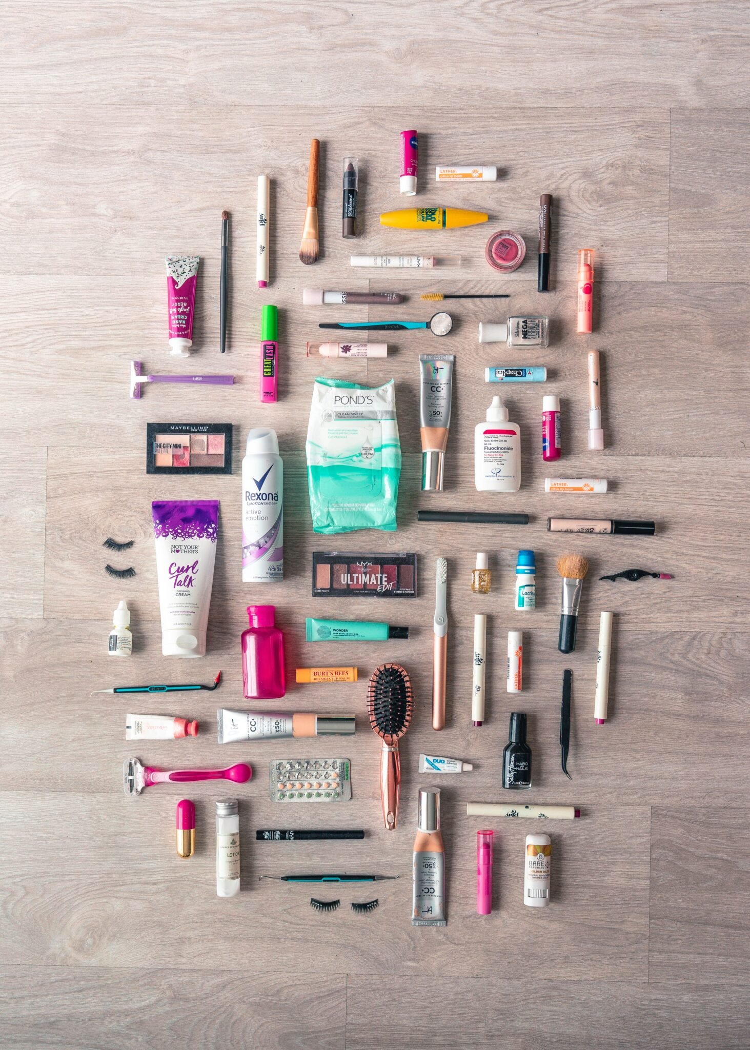 A diverse collection of beauty and grooming products neatly arranged on a wooden surface in a flatlay style.